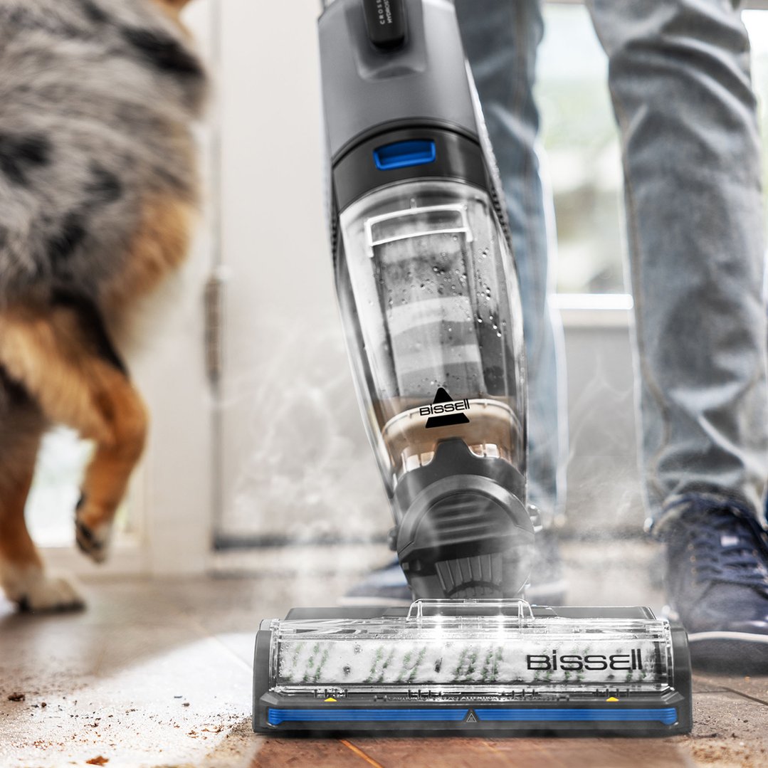 Vacuum cleaner cleaning a dirty floor with a dog and person in the background
