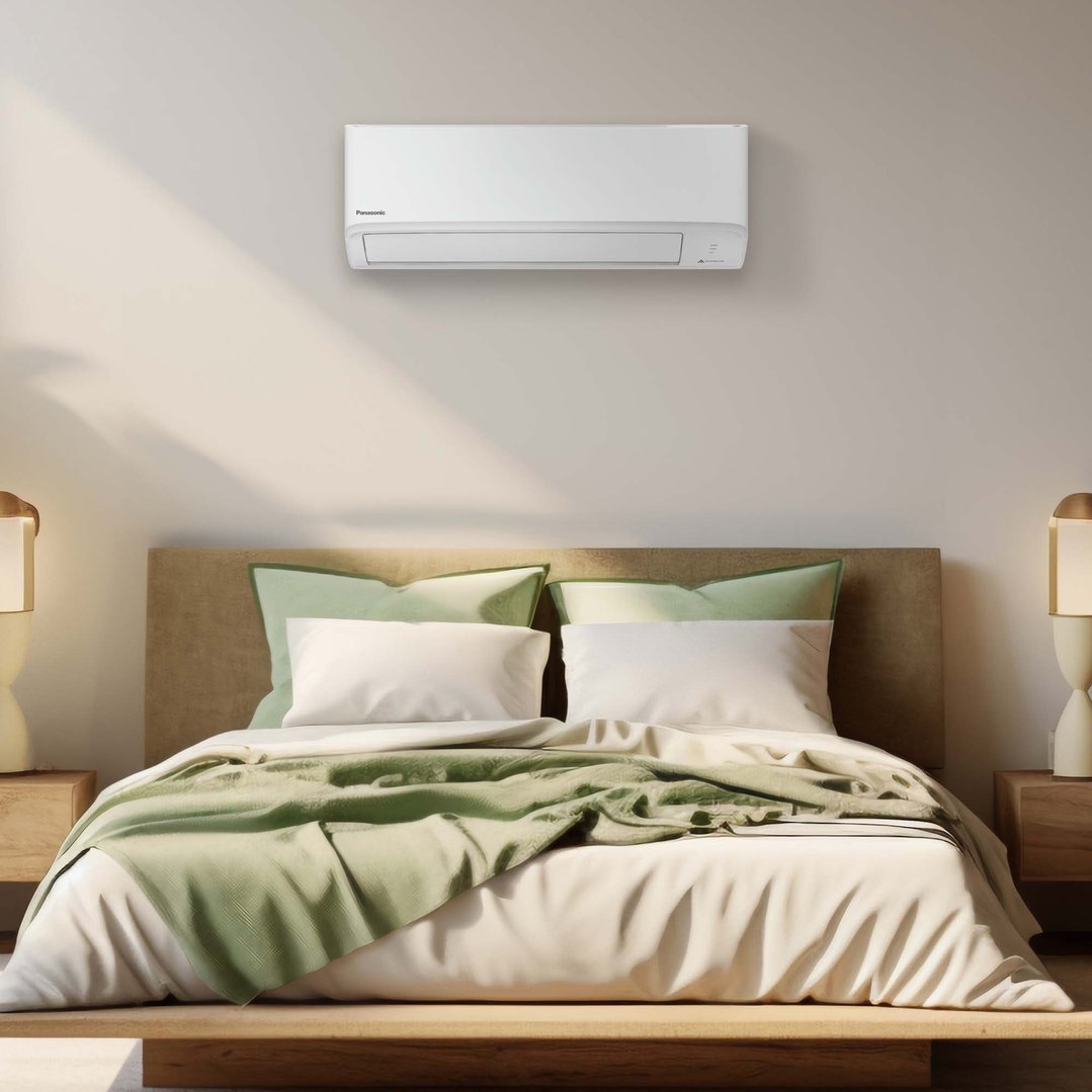A white Panasonic air conditioner mounted on a wall above a bed in a bedroom
