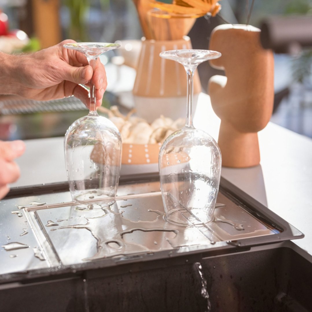 Hands placing a wine glass on a wet Extension Drainer over a sink