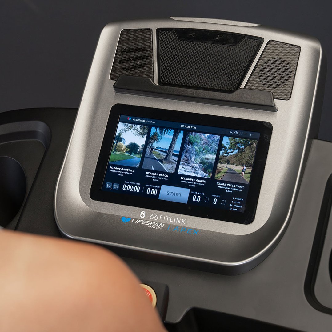 Person's arm near the console of a treadmill displaying virtual run options