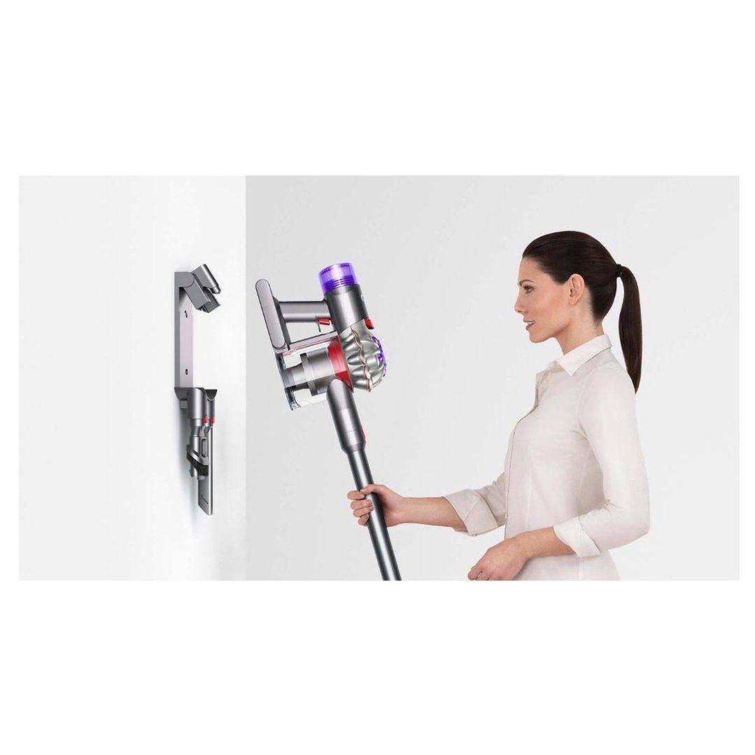 Woman holding a Dyson handstick vacuum cleaner next to its wall-mounted dock