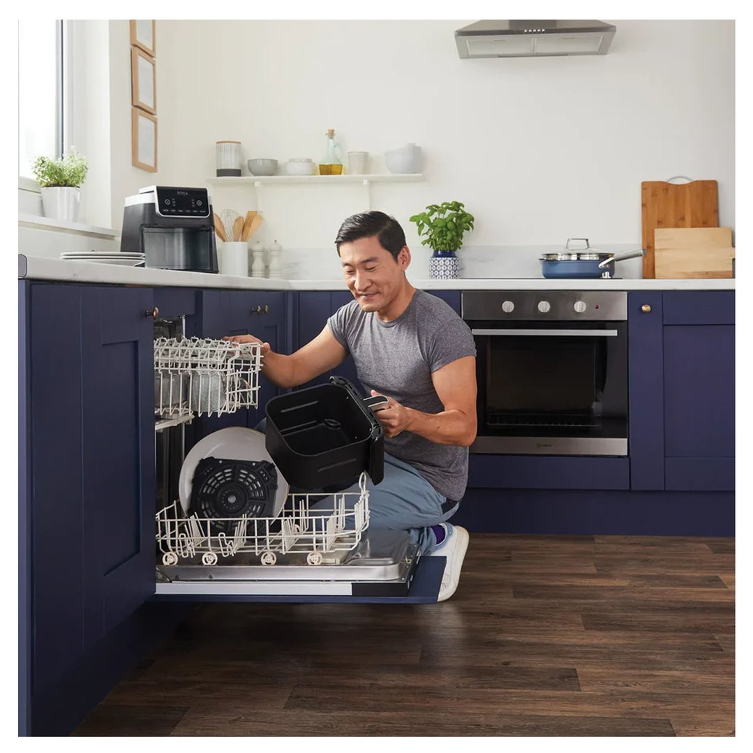 Man loading an air fryer basket into a dishwasher in a modern kitchen