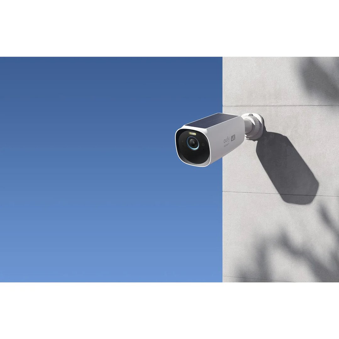 Security camera mounted on a white wall against a clear blue sky