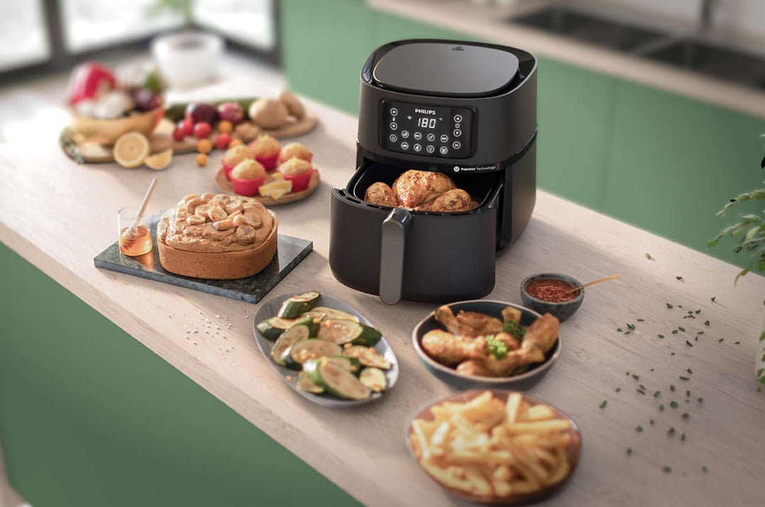 Black Philips airfryer on a kitchen counter with various cooked foods