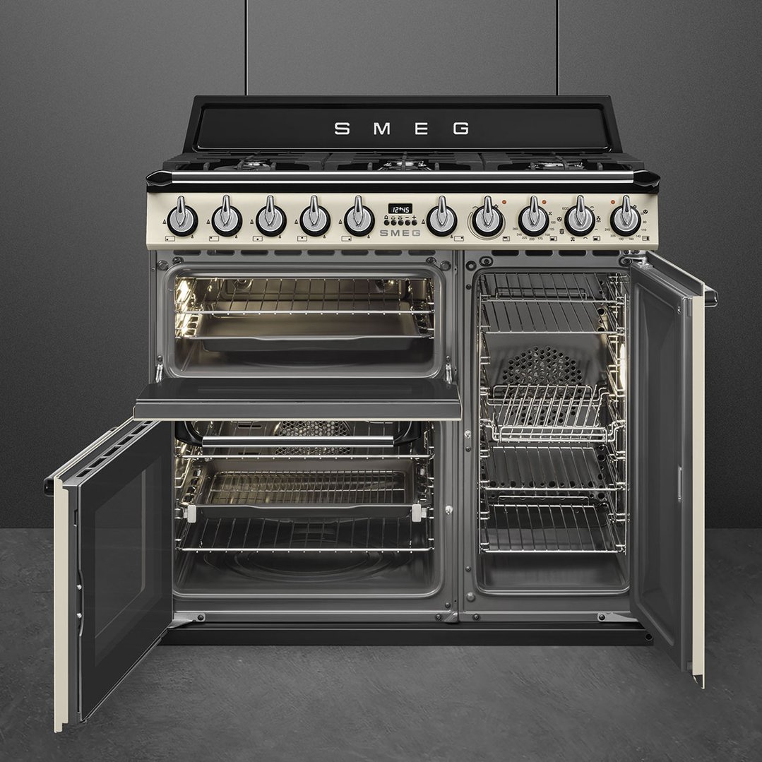 Smeg freestanding oven with multiple compartments and doors open in a dark kitchen