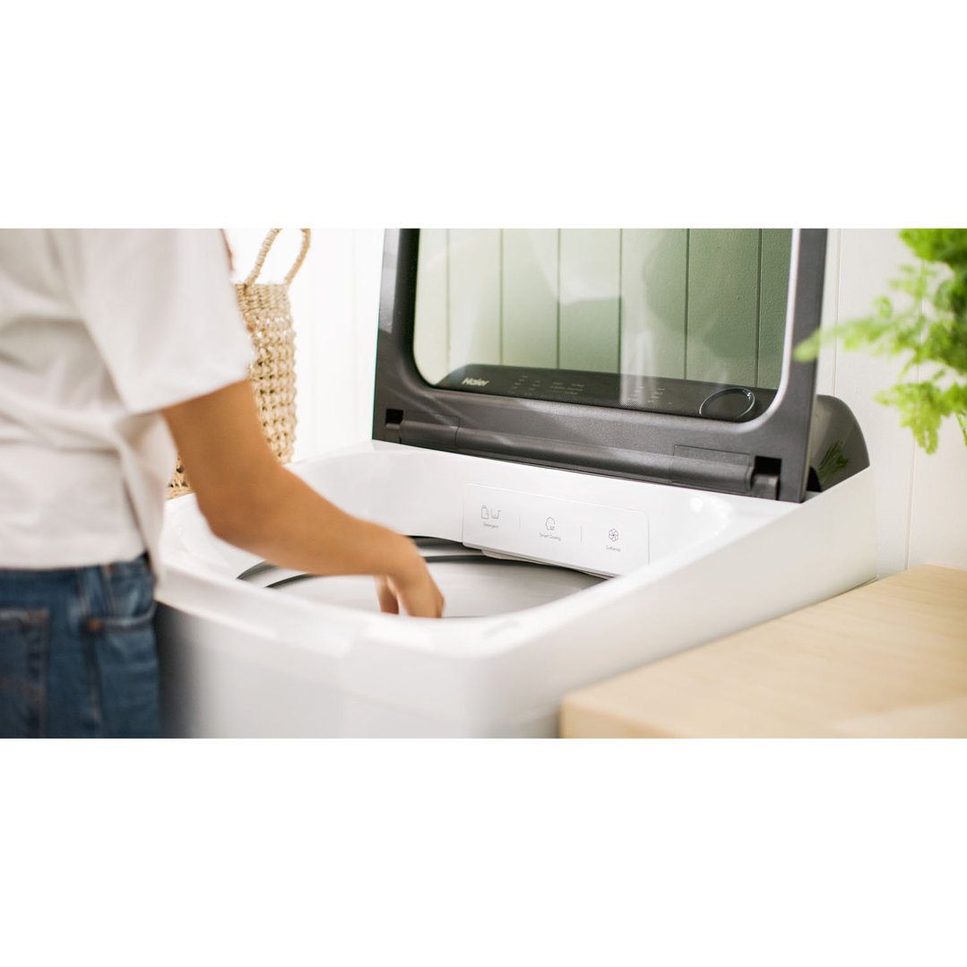 Person loading laundry into a white Haier top loader washing machine