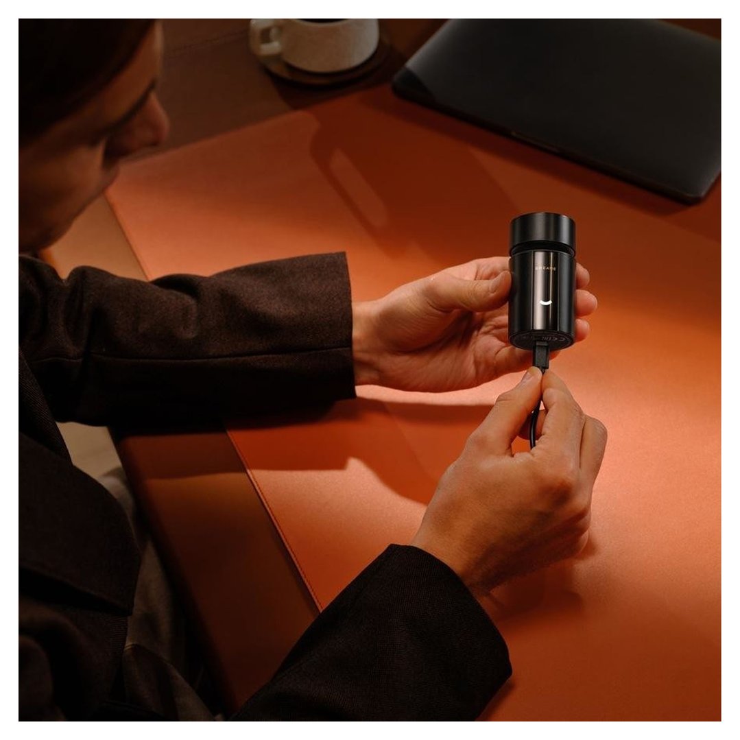 Person holding a black shaver and plugging in a charging cable