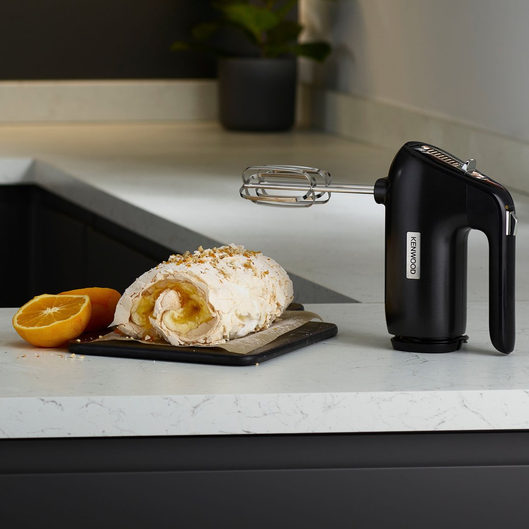 Black KENWOOD hand mixer on a kitchen counter next to a meringue roll