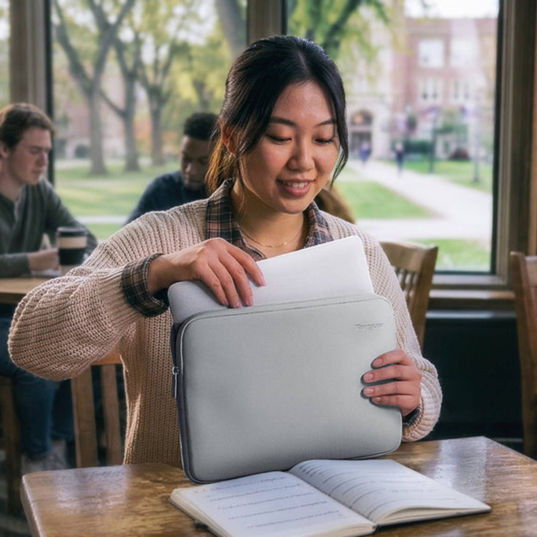 Woman placing a laptop into a grey laptop sleeve at a wooden table