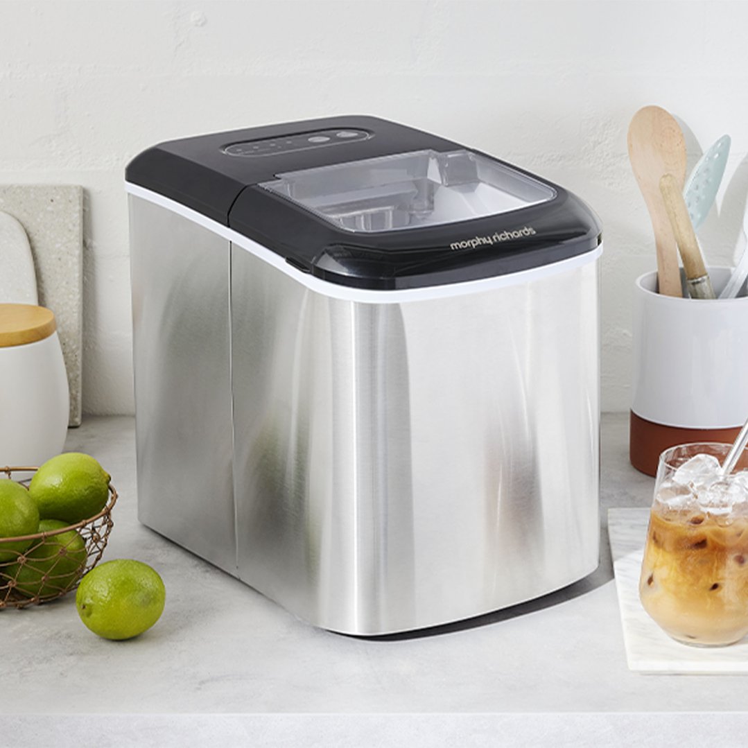 Stainless steel ice maker on a kitchen counter with limes and iced coffee