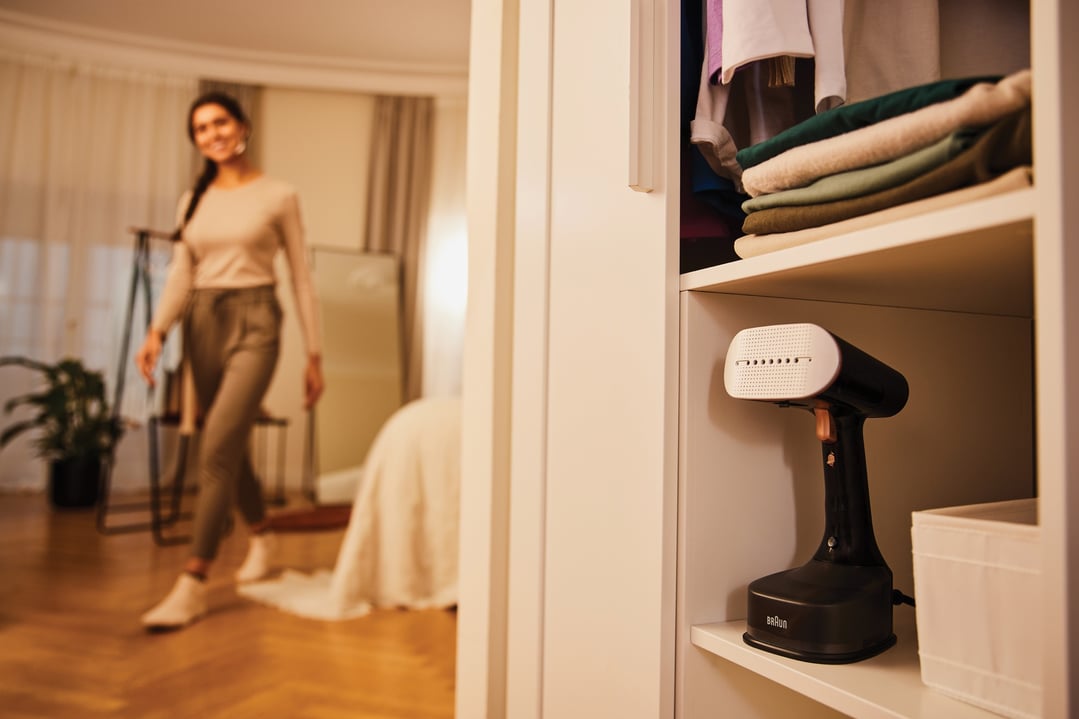 Braun Garment Steamer on a shelf in a closet, with a woman walking in the background
