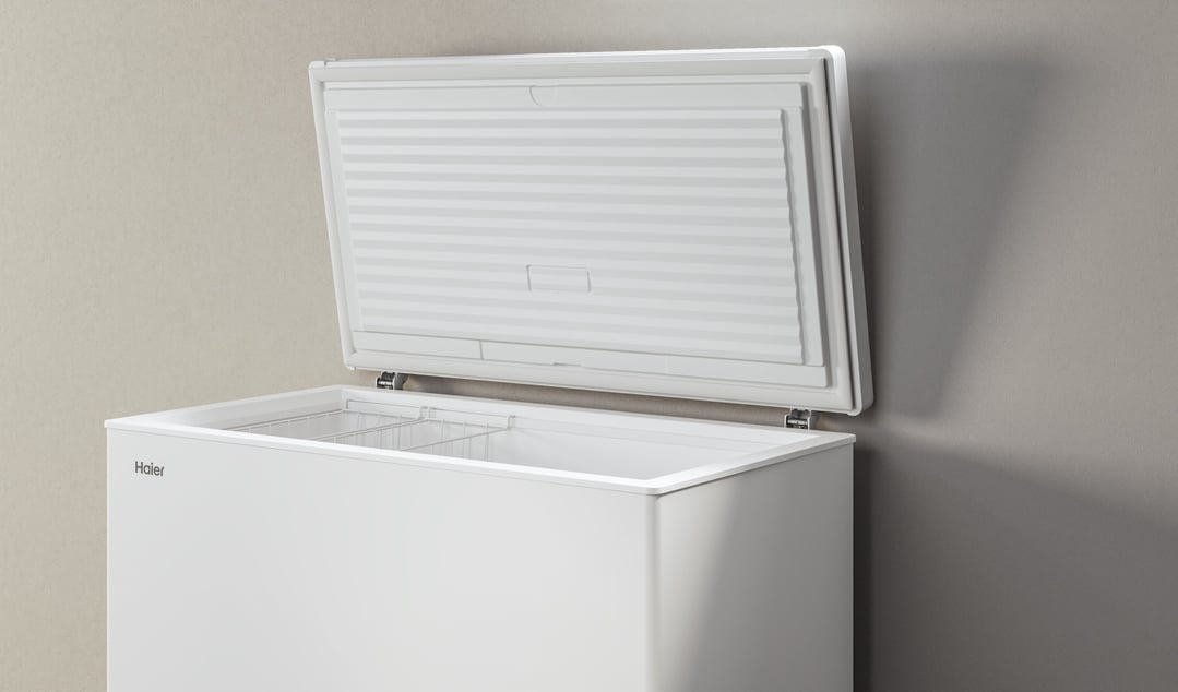 White Haier chest freezer with the lid open, against a neutral wall
