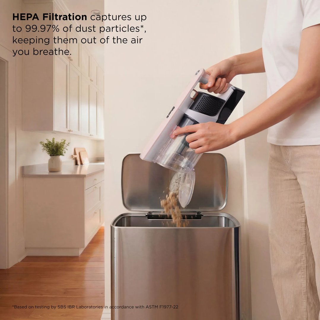 Person emptying a Shark handstick vacuum into a stainless steel bin