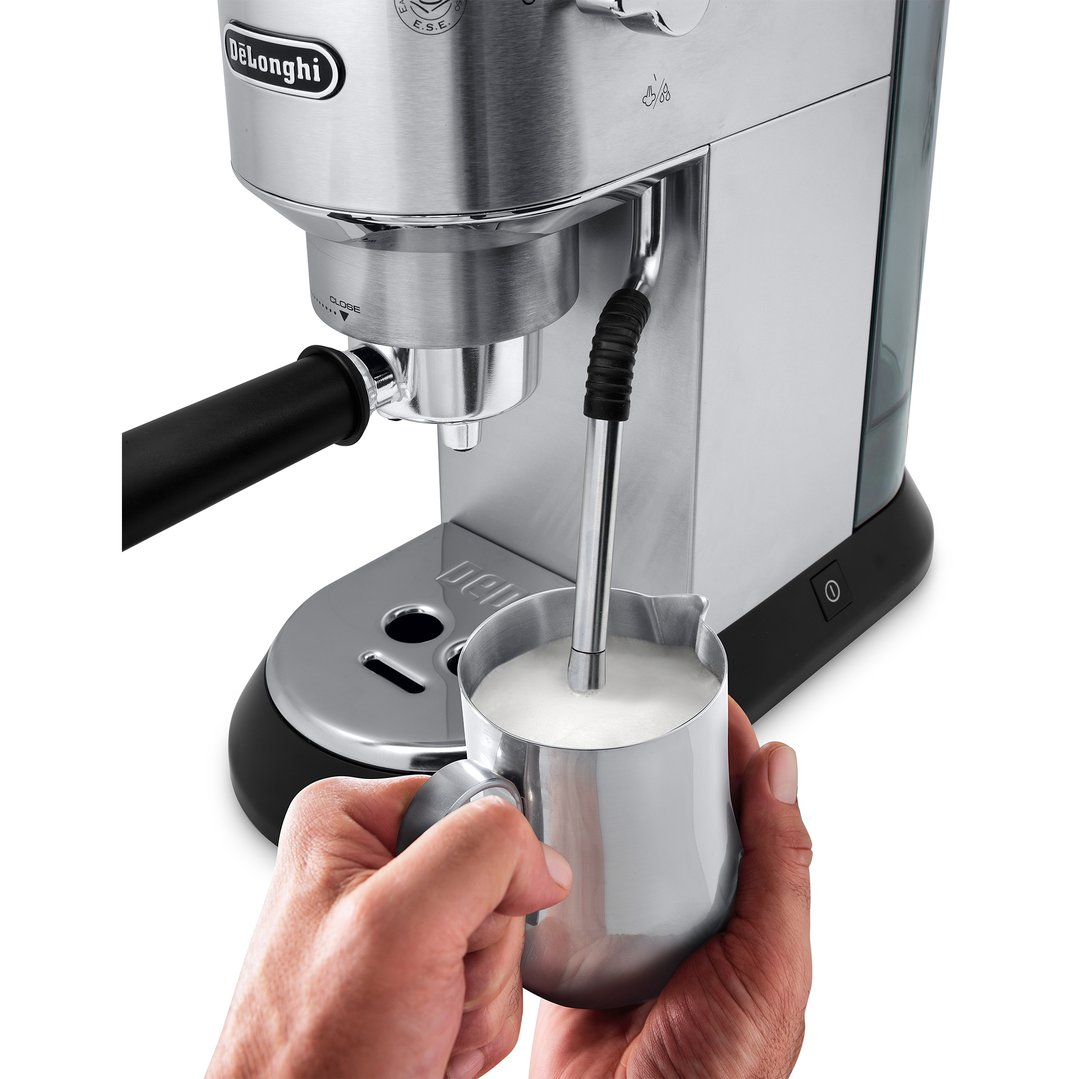 Hands holding a milk jug under the steam wand of a coffee machine
