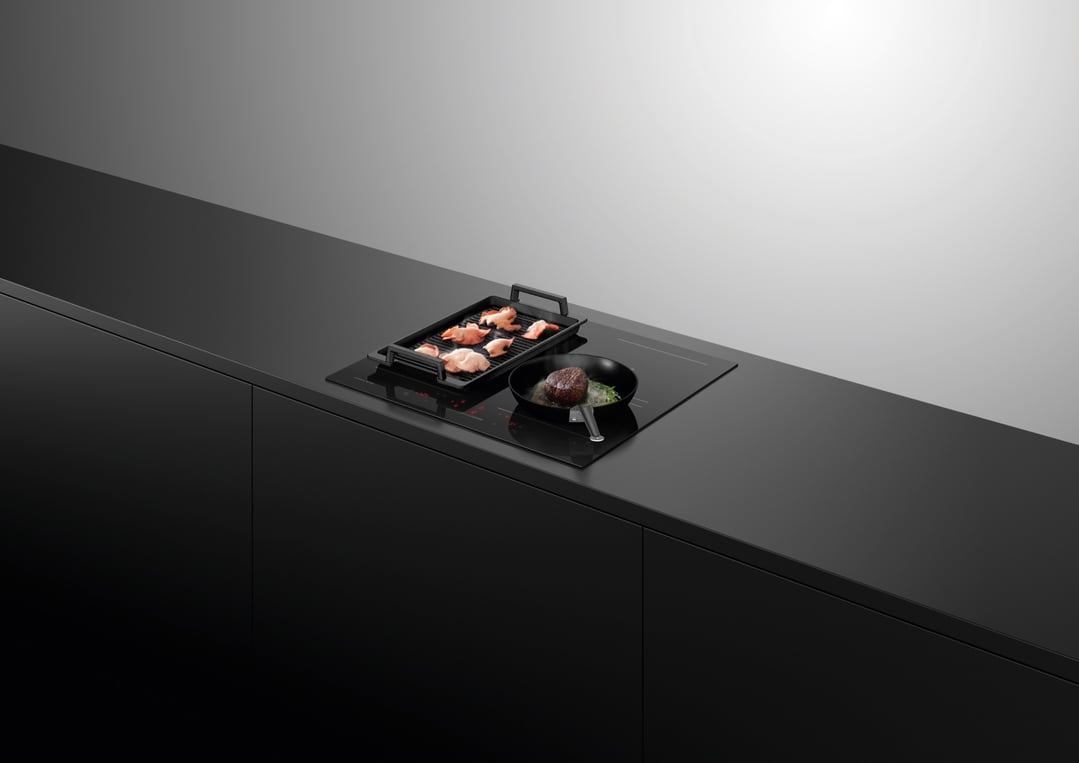 Induction cooktop with a grill plate and frying pan cooking food in a modern kitchen