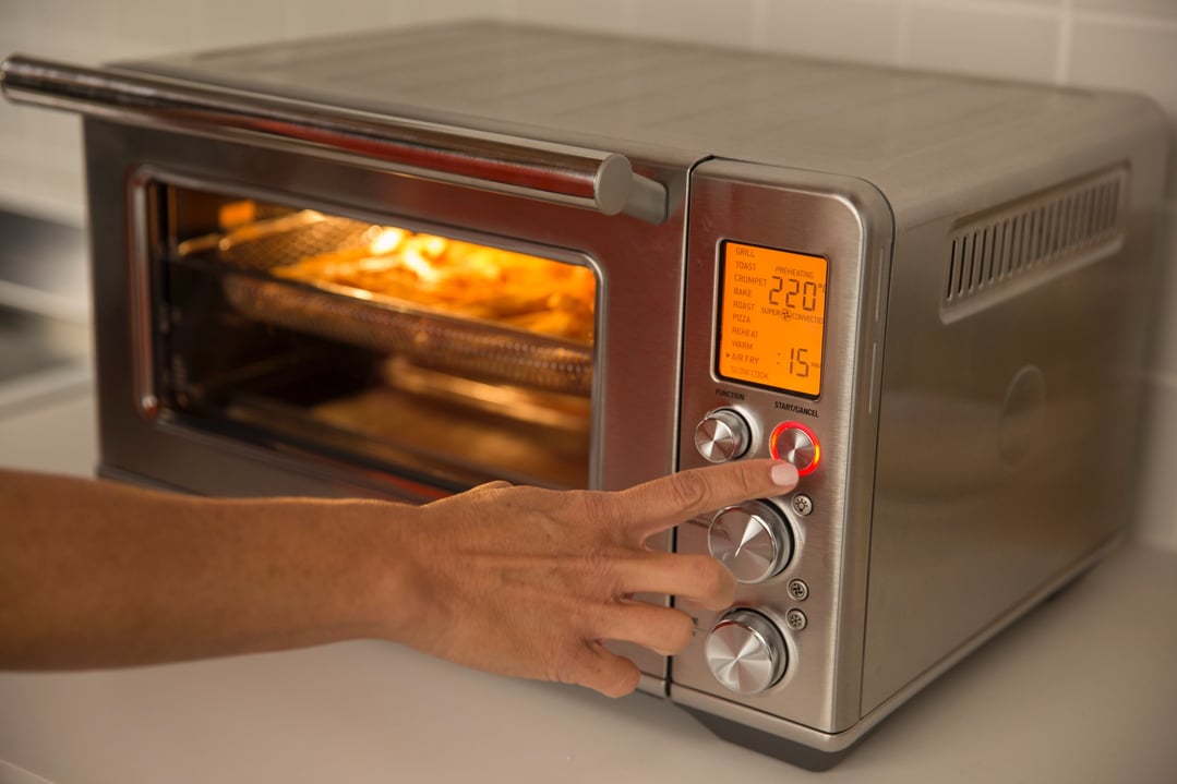 Hand pressing the start button on a Breville Smart Oven Air Fryer
