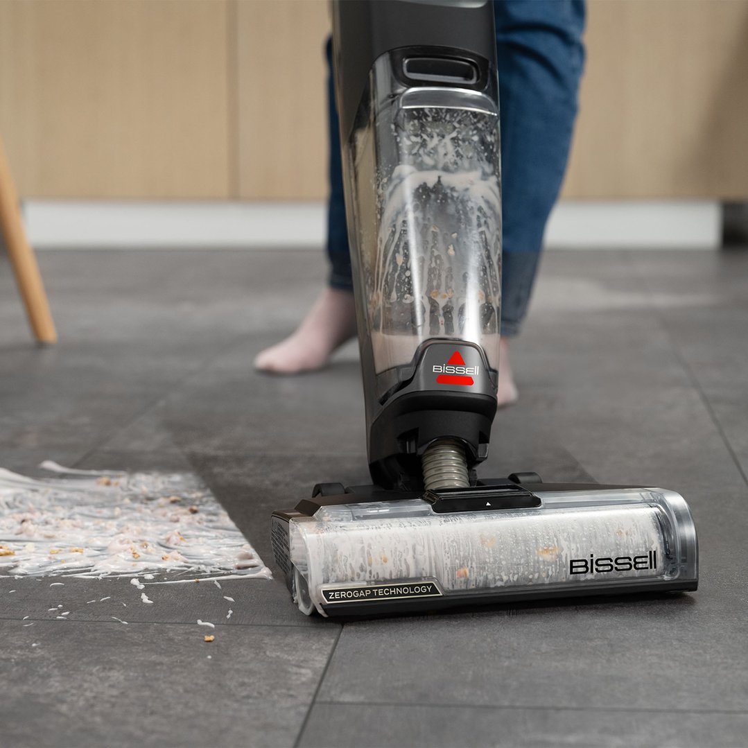 A Bissell vacuum cleaner cleaning a messy floor in a kitchen setting
