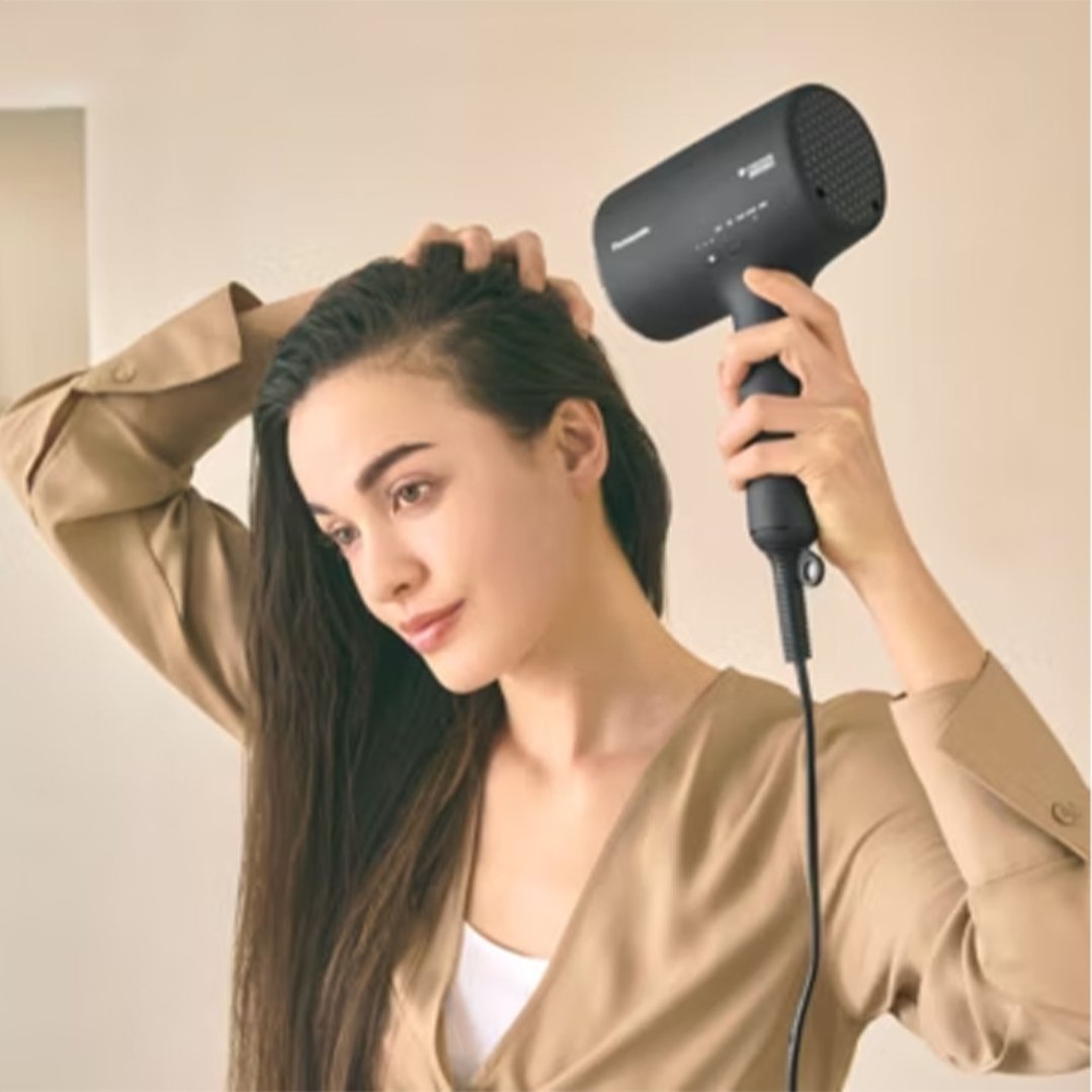 Woman drying her long hair with a black Panasonic hair dryer