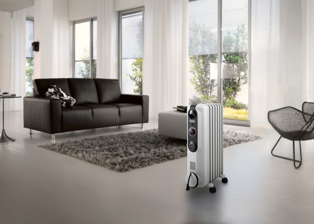 White oil column heater in a modern living room with a black sofa