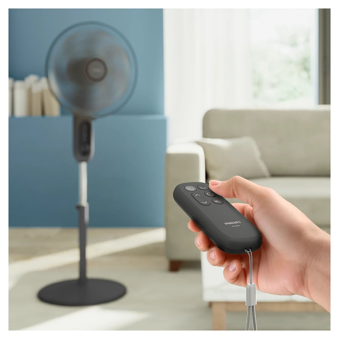 Hand holding a remote control for a pedestal fan in a living room