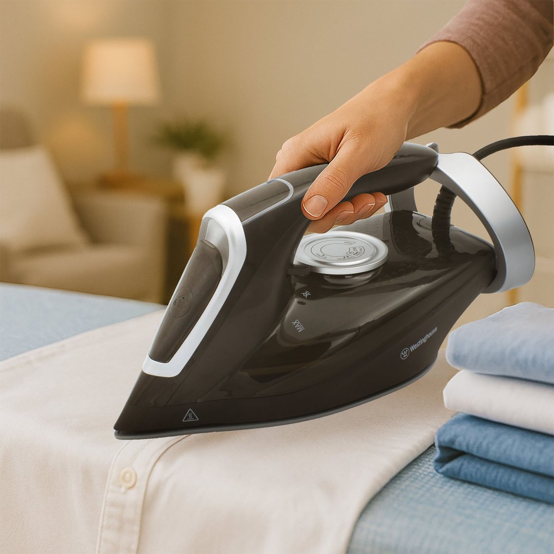 Hand ironing a light-colored shirt with a black and silver steam iron