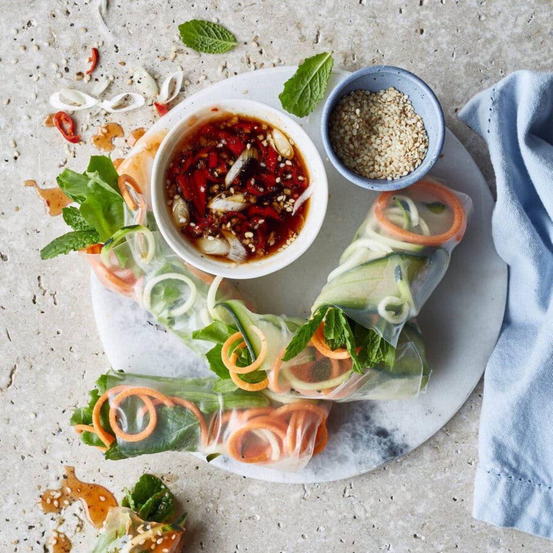 Fresh spring rolls with vegetables and herbs, served with dipping sauce and sesame seeds