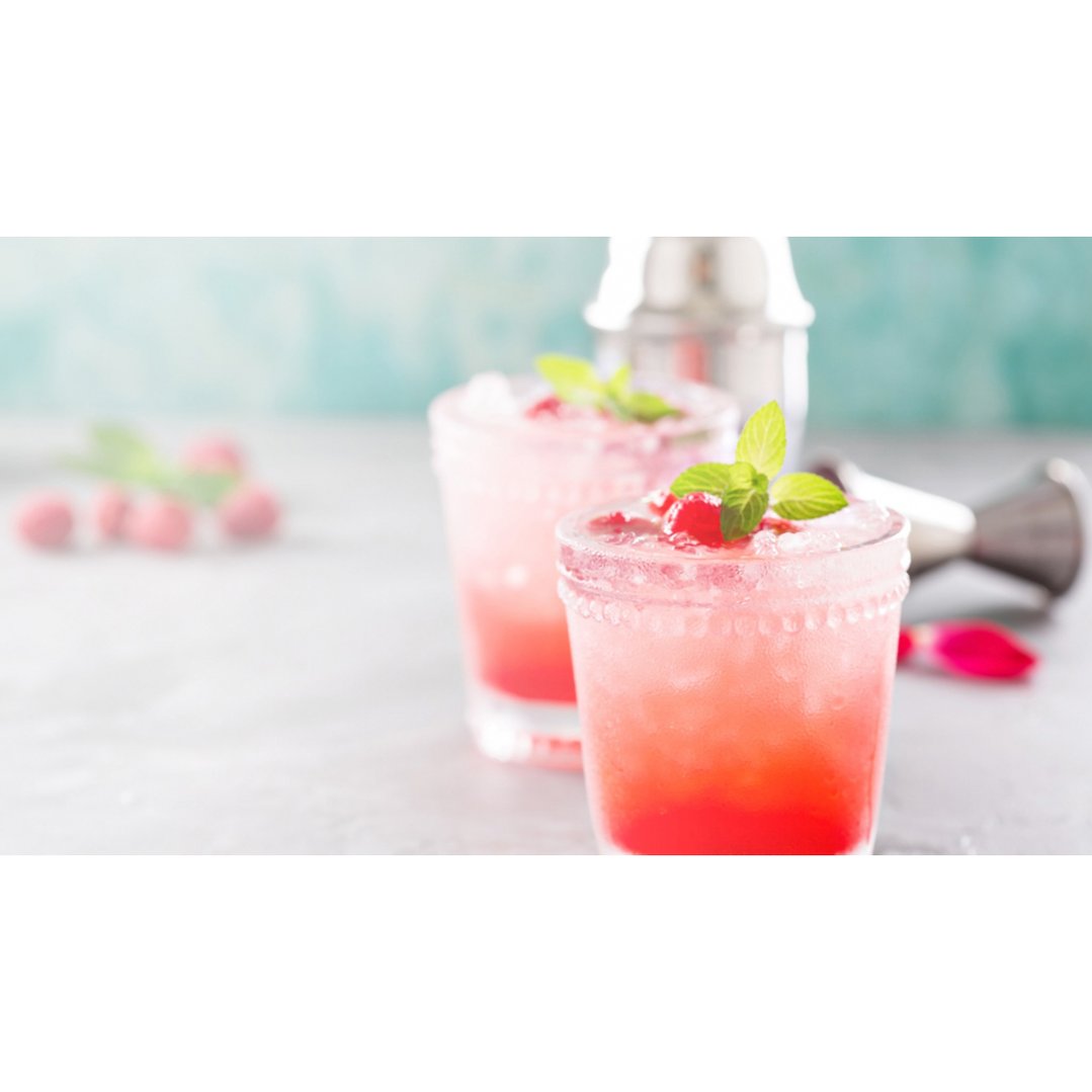 Two glasses of pink drink with mint and berries on a counter