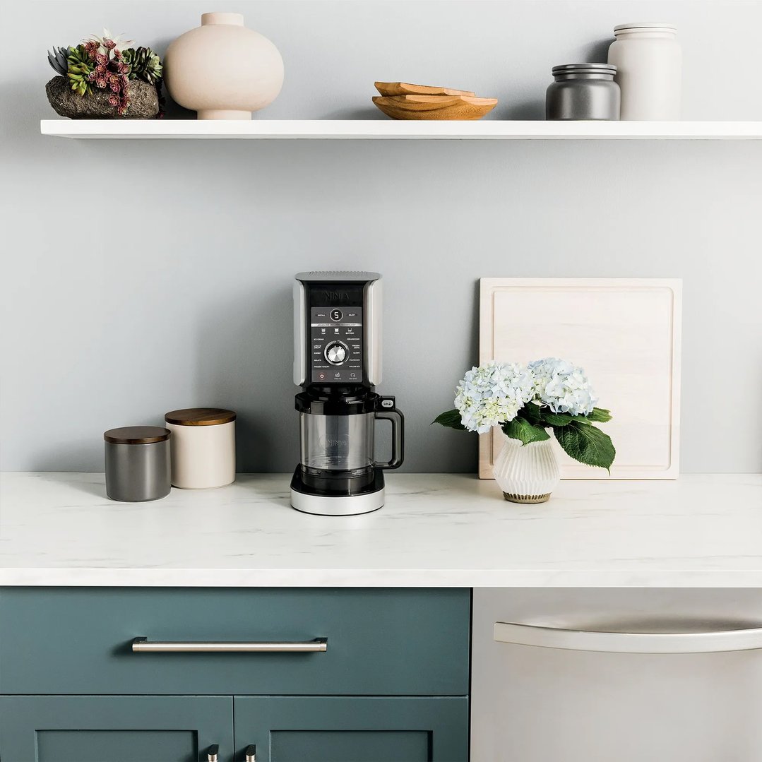 Ninja ice cream maker on a kitchen counter with decorative items and shelves