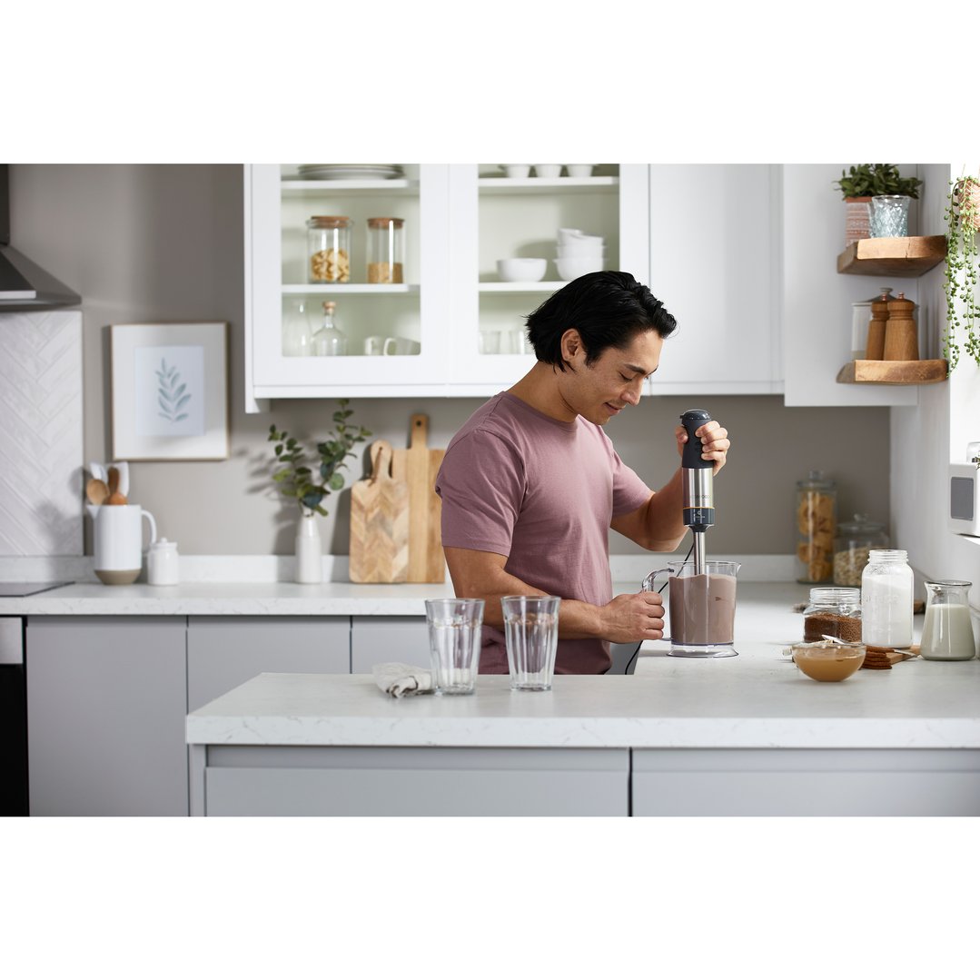Man using a hand blender to mix a drink in a modern kitchen
