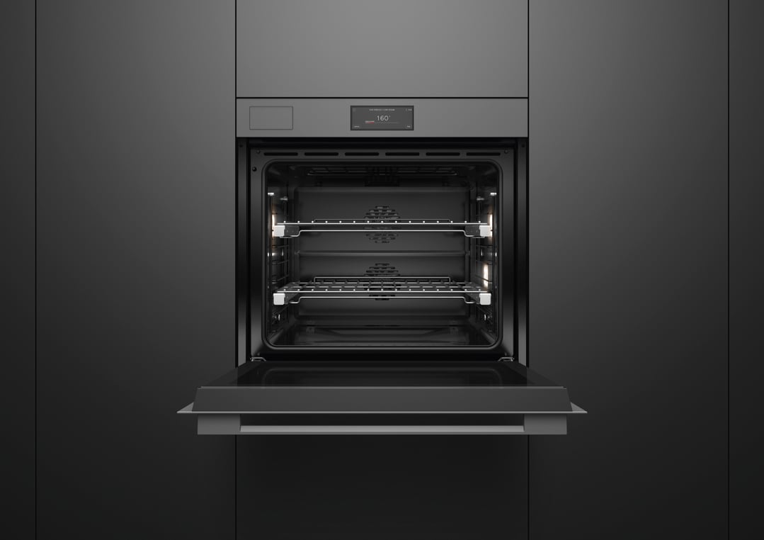 Open grey glass oven with interior lights on in a dark kitchen