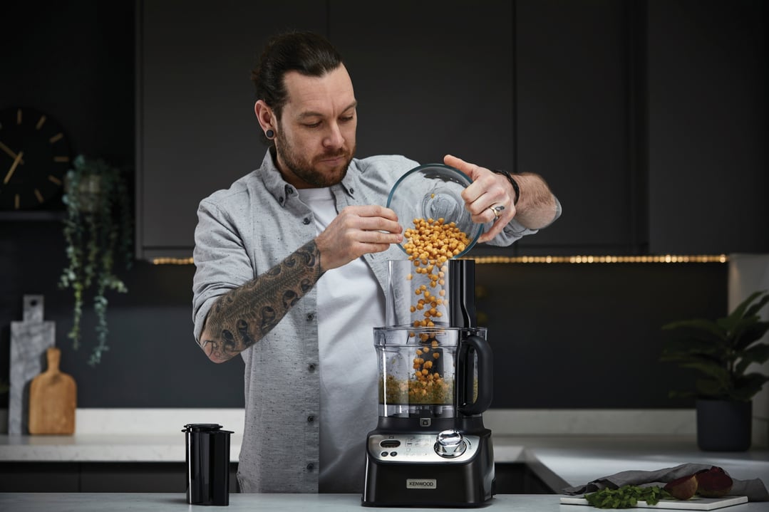 Man pouring chickpeas into a Kenwood food processor in a modern kitchen