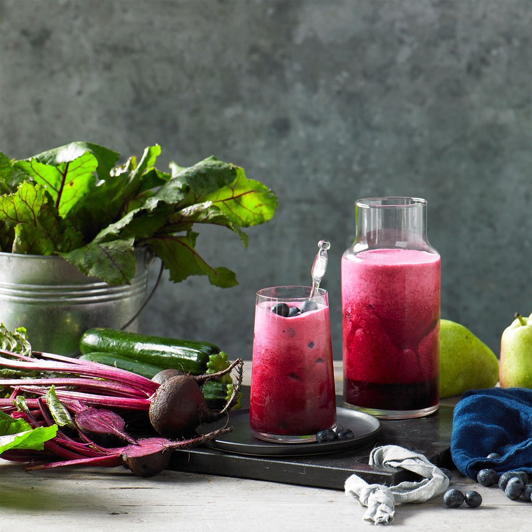 Two glasses of red juice with fresh beets, zucchini, blueberries, and pears