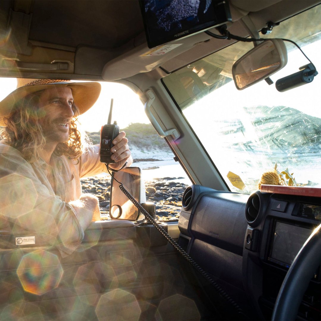 Man in a car holding a Uniden UHF handheld radio at the beach