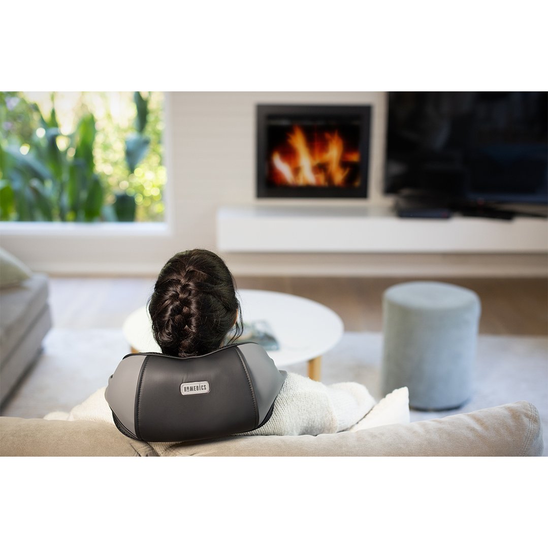 Woman wearing a neck massager while relaxing on a sofa in a living room