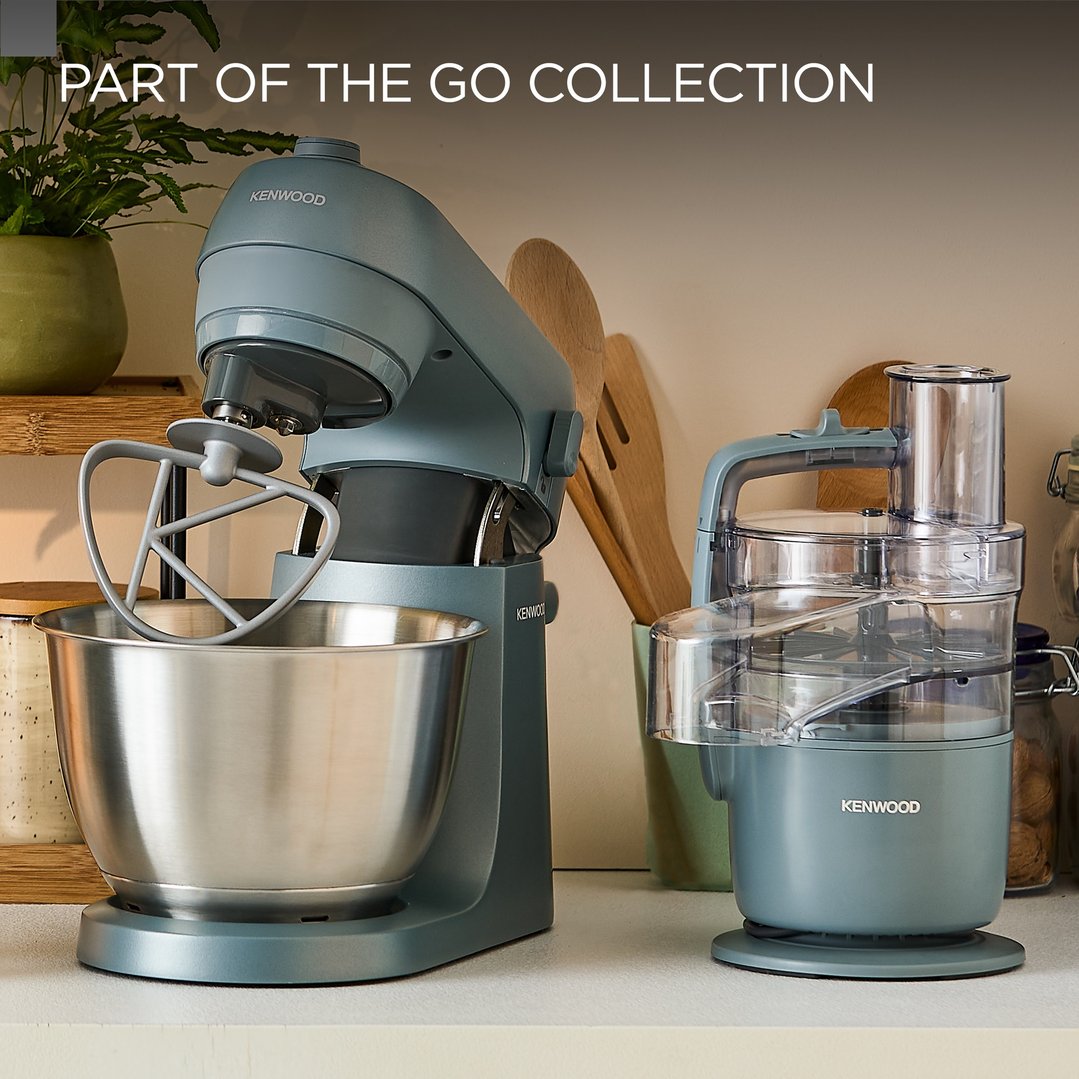 Two Kenwood food mixers on a kitchen counter with a plant and wooden utensils