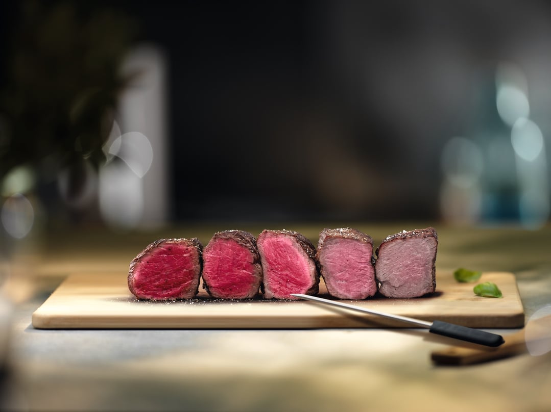 Five cuts of beef on a wooden board with a food probe