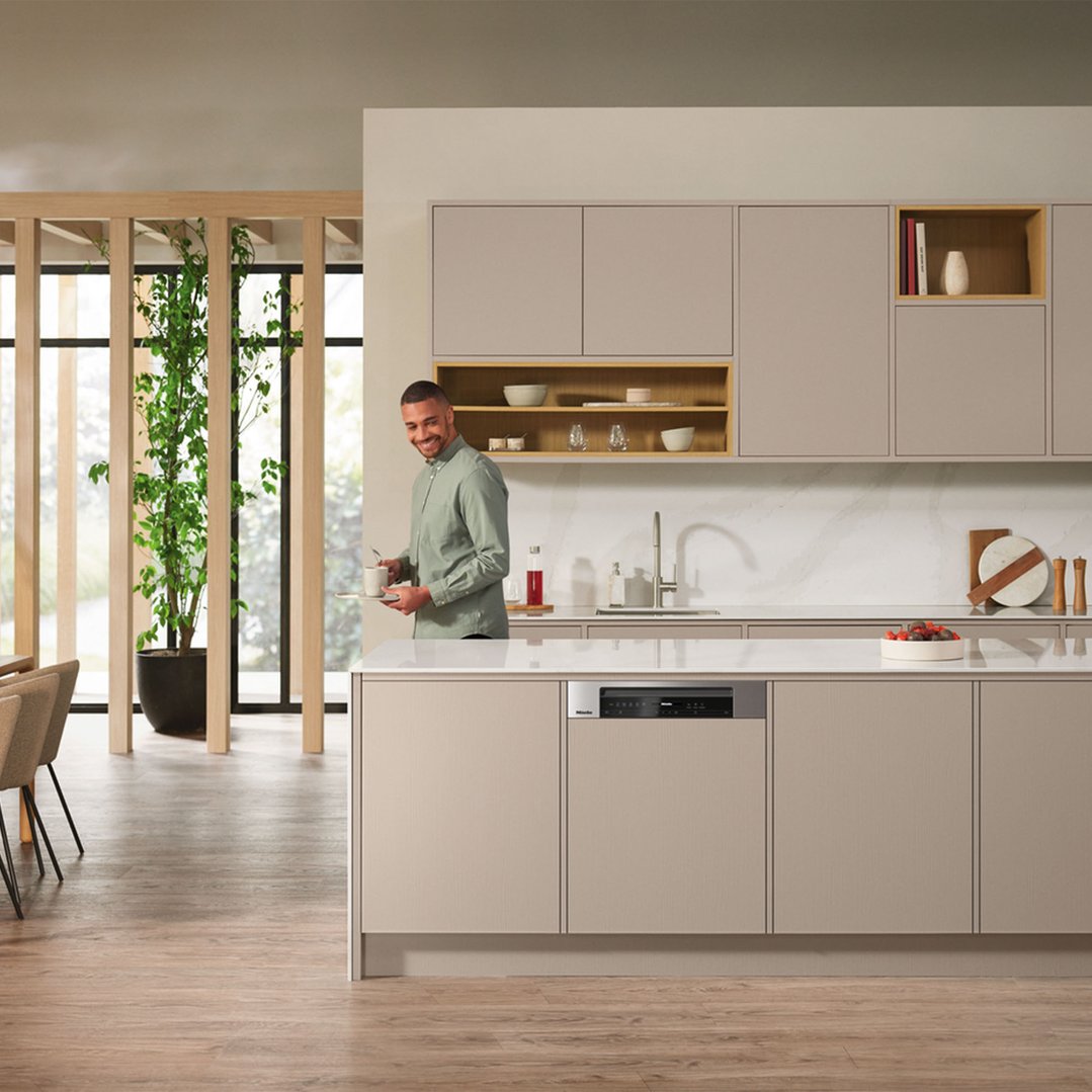 Man holding a tray with a cup in a modern kitchen with a dishwasher