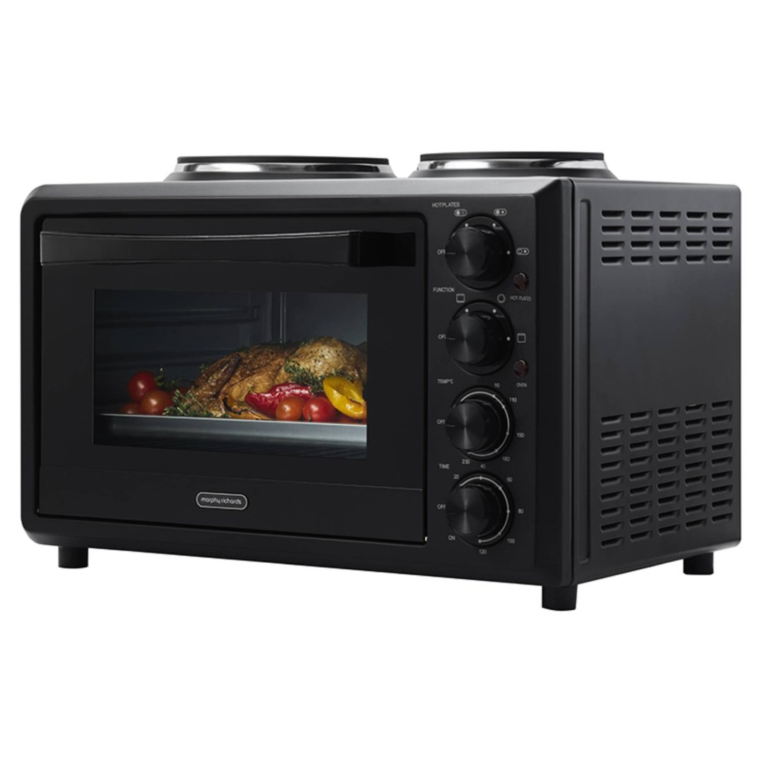 Black benchtop convection oven with hot plates, cooking a whole chicken and vegetables
