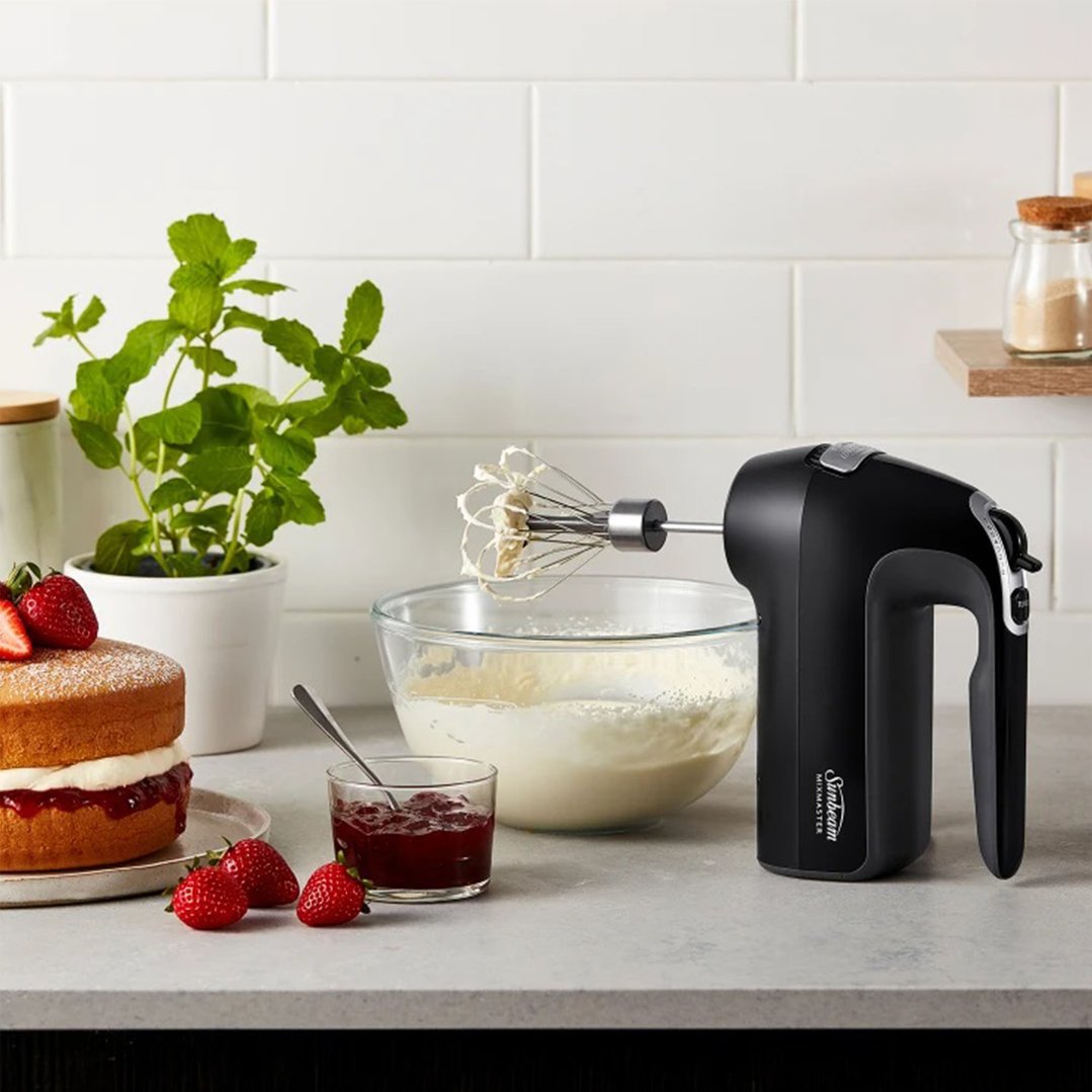 Black Sunbeam Mixmaster Hand Mixer Pro mixing cream in a glass bowl on a counter