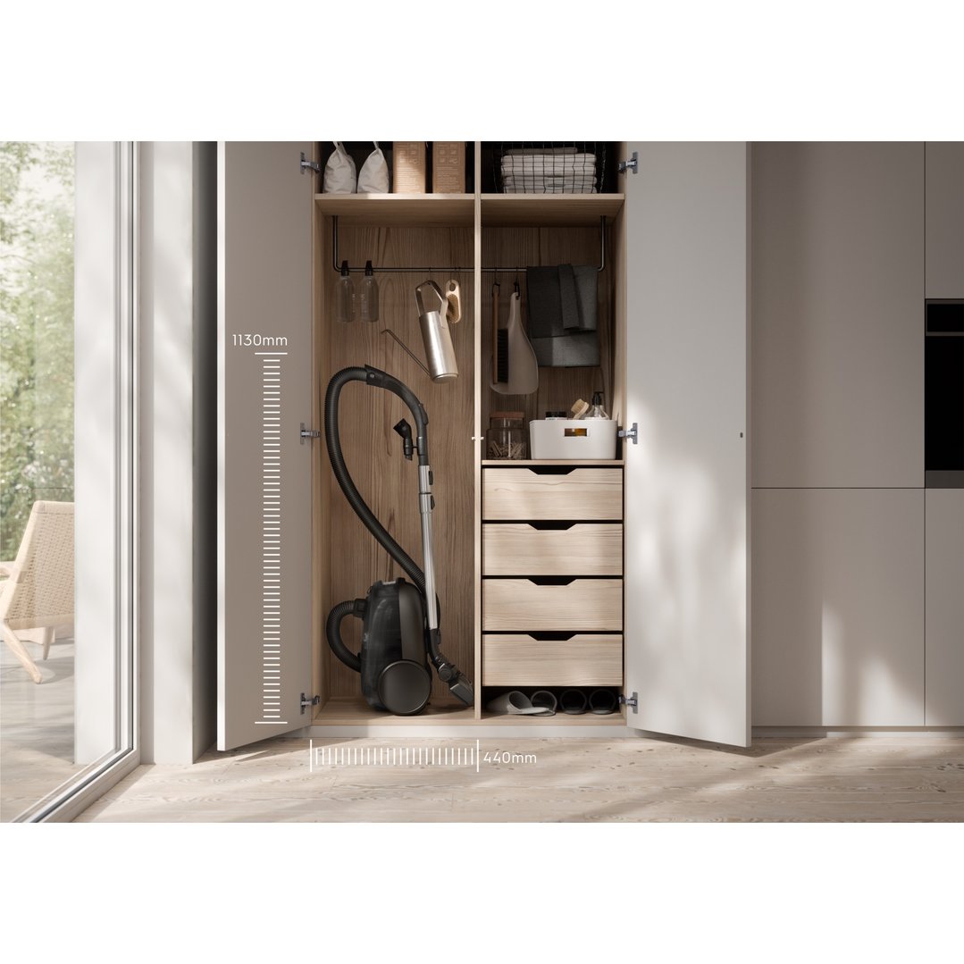 Black canister vacuum cleaner stored in a wooden cabinet with drawers