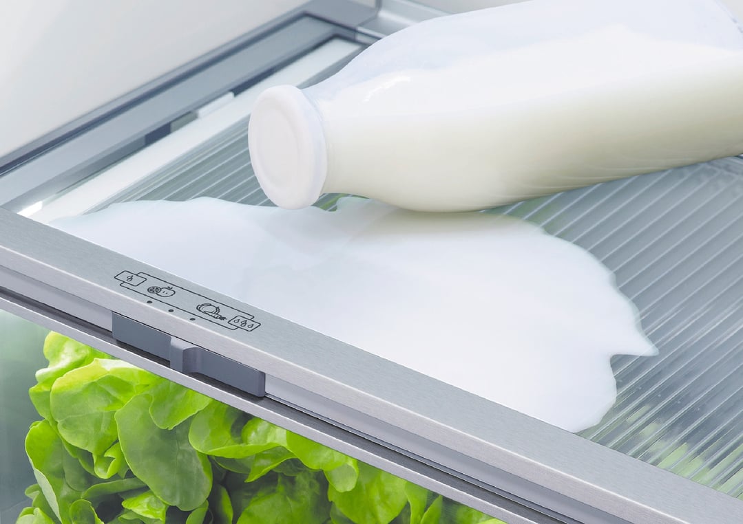 Spilled milk from a bottle inside a refrigerator, with lettuce visible below