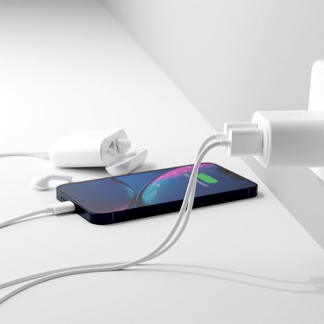 White dual port wall charger plugged in, charging a phone and earbuds