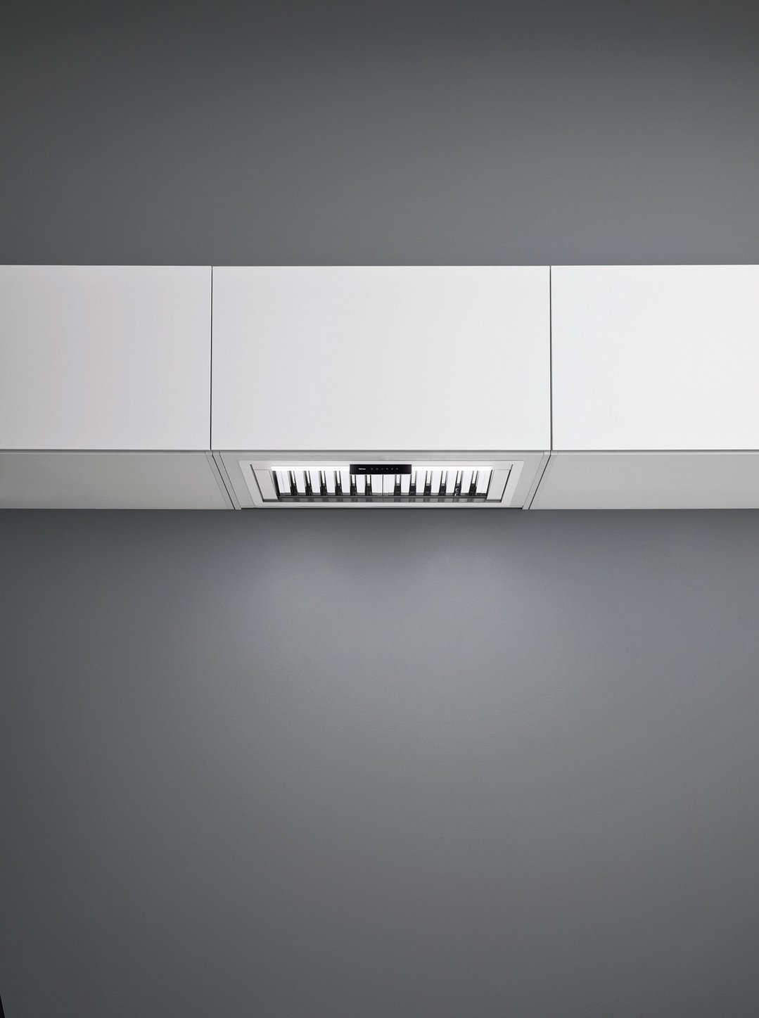 Undermount rangehood integrated into white kitchen cabinetry with a dark grey wall