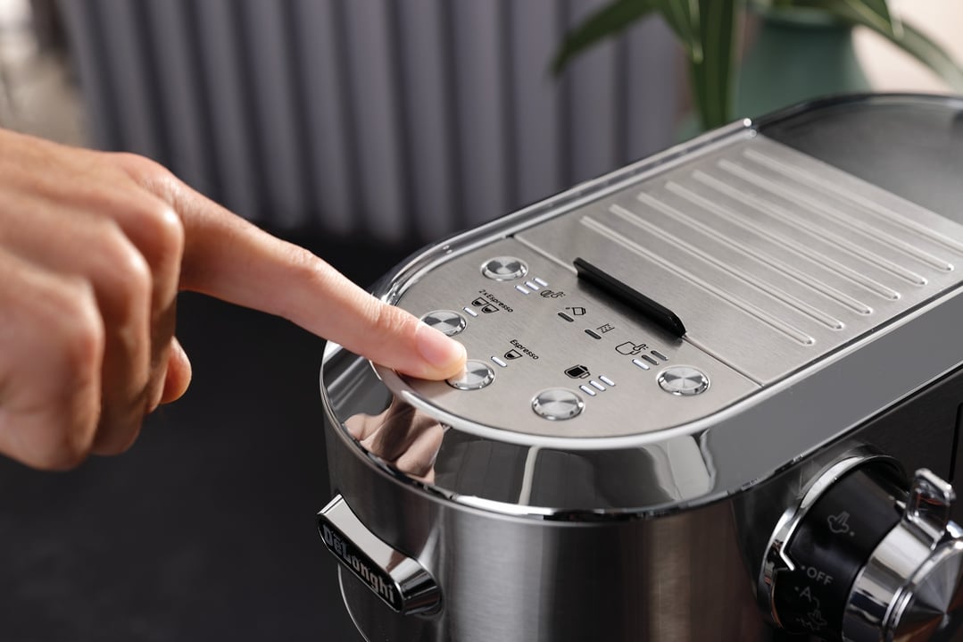Hand pressing a button on the top of a DeLonghi coffee machine