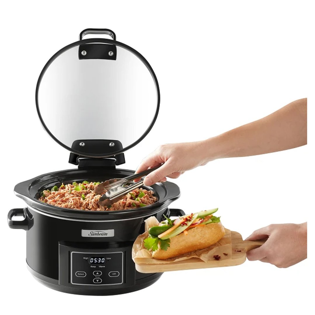 Hand serving food from a Sunbeam slow cooker with a sandwich on a wooden board