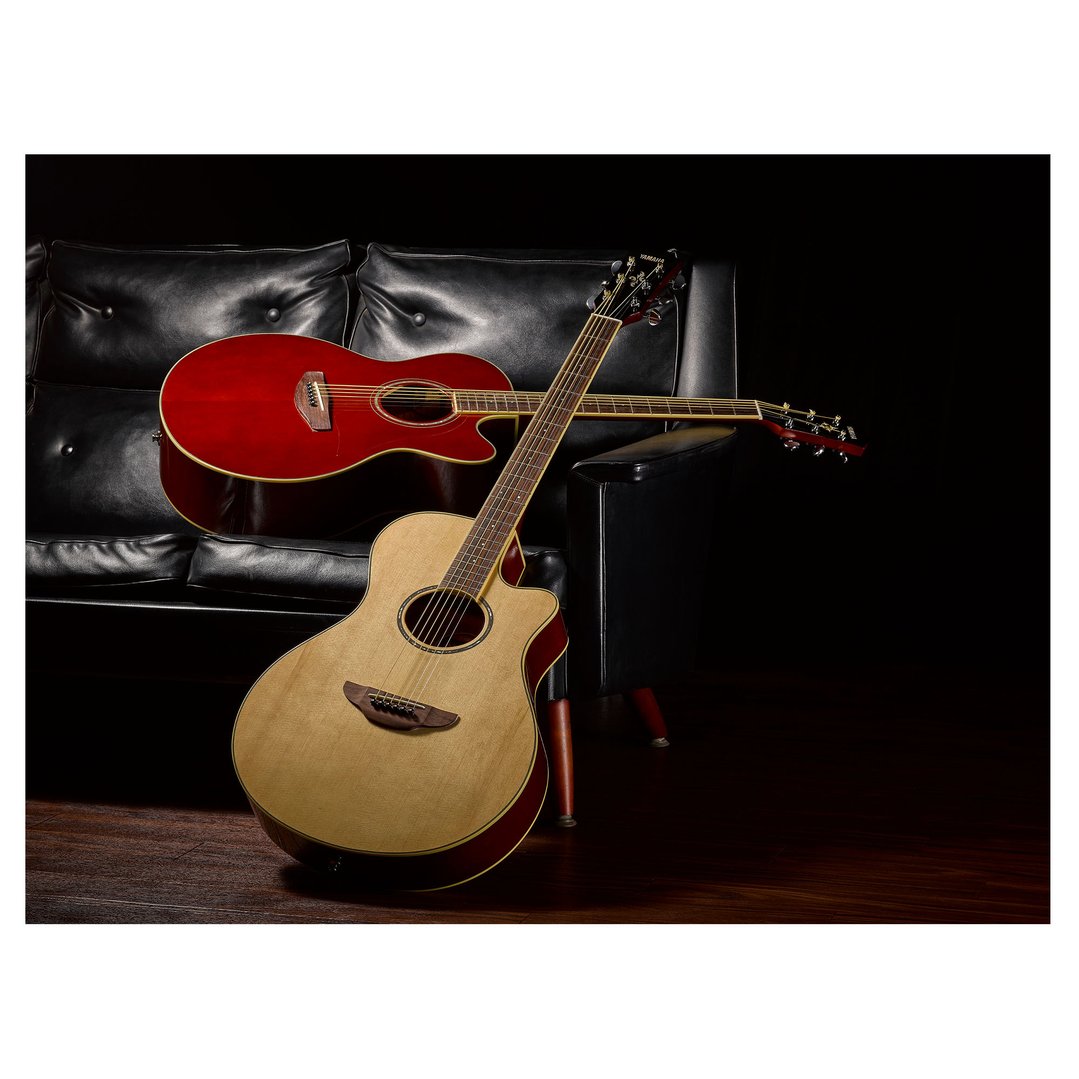Two acoustic electric guitars, one red and one natural wood, leaning against a black leather couch