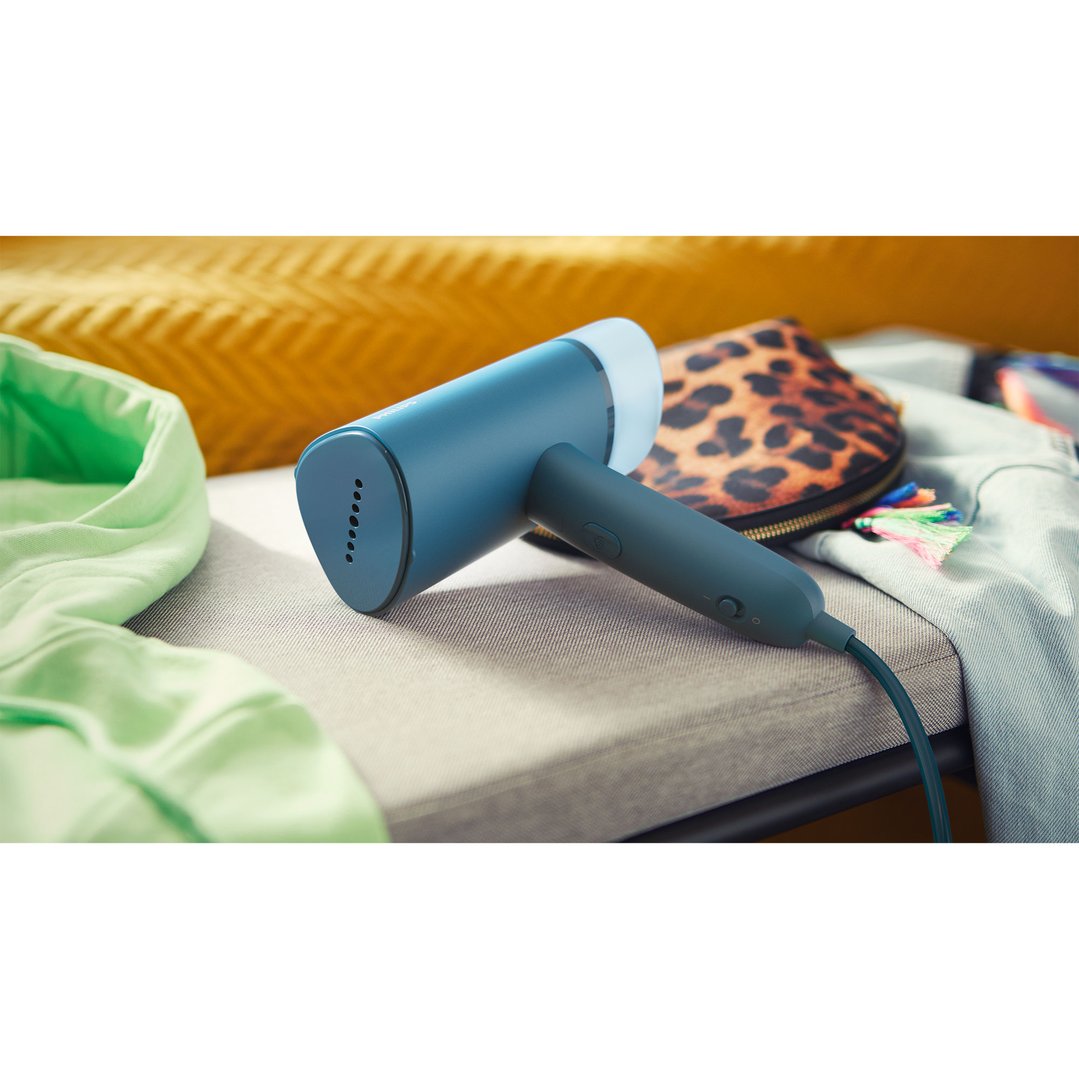 Blue handheld garment steamer on a textured surface with clothes and bag