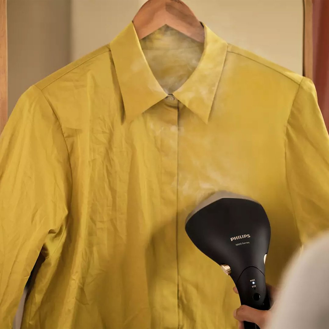 Handheld Garment Steamer steaming a yellow shirt on a wooden hanger