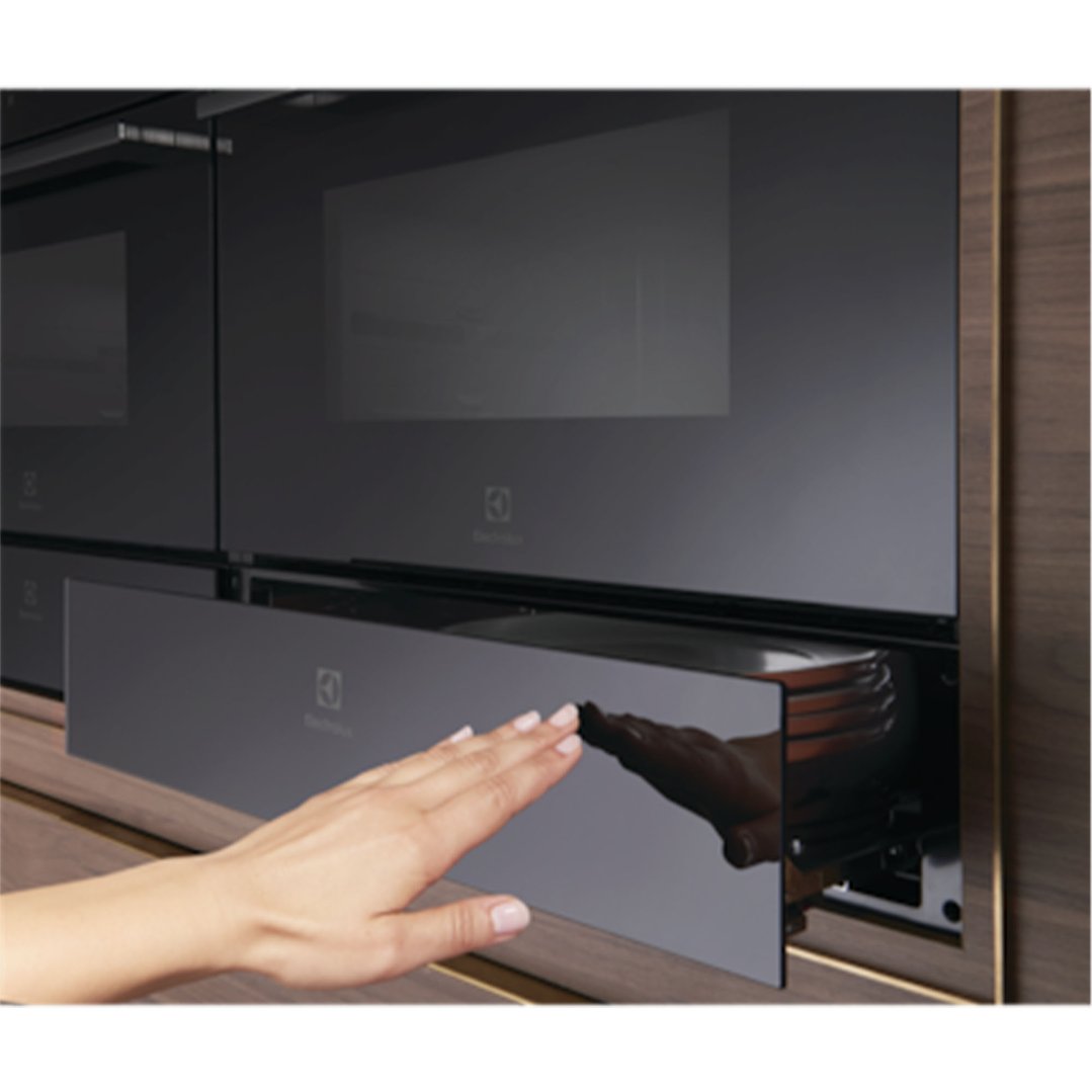 Hand opening a built-in warming drawer in a kitchen setting