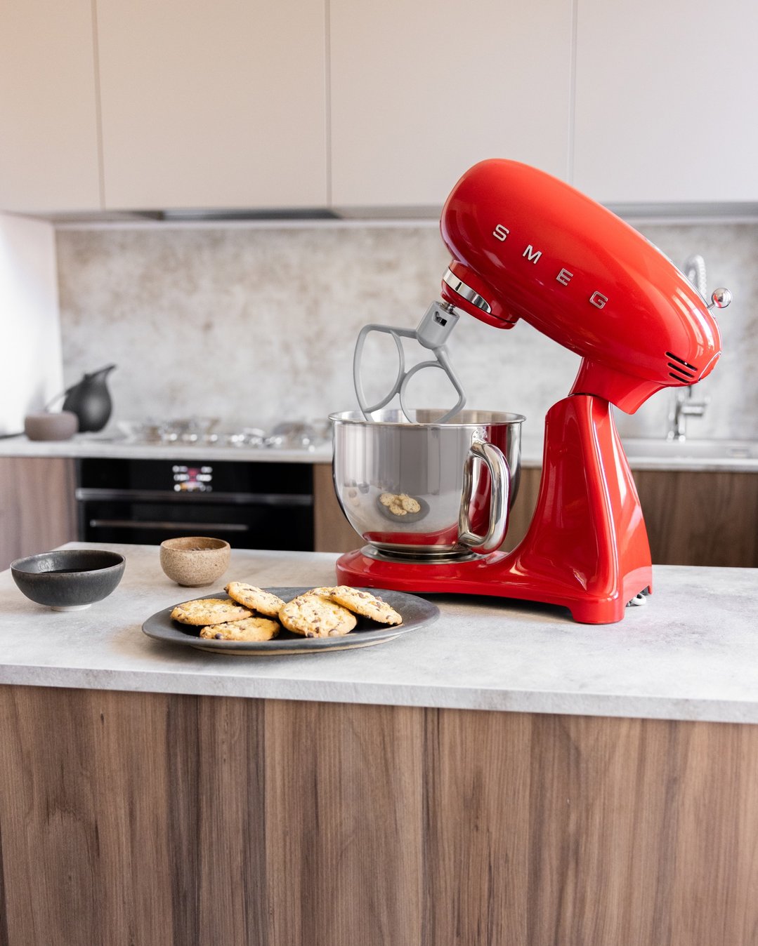 Red Smeg stand mixer on a kitchen counter with cookies and bowls